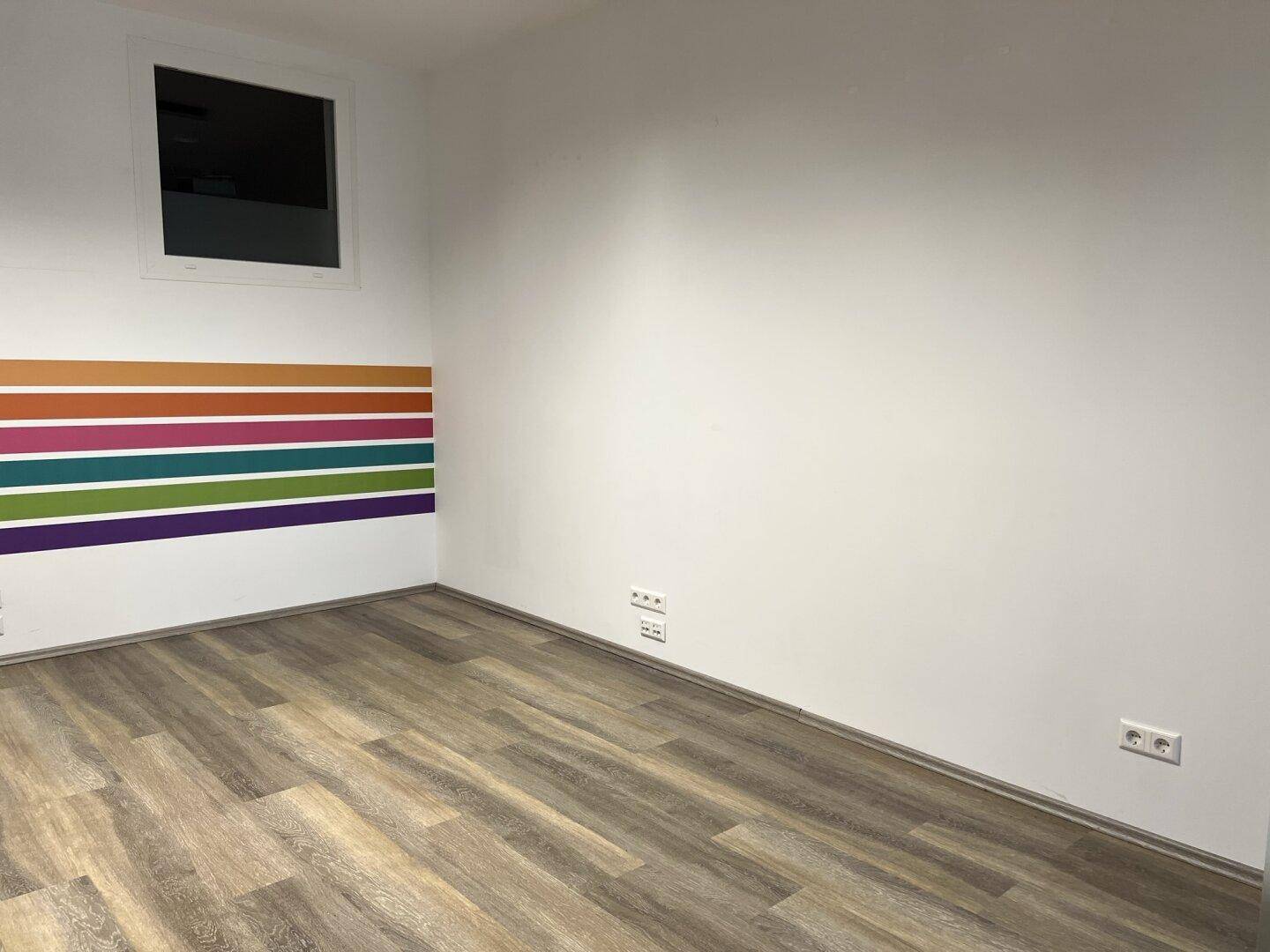 Eckbereich eines Büros mit Laminatboden und einer farbigen Akzentwand, ausgestattet mit Steckdosen.