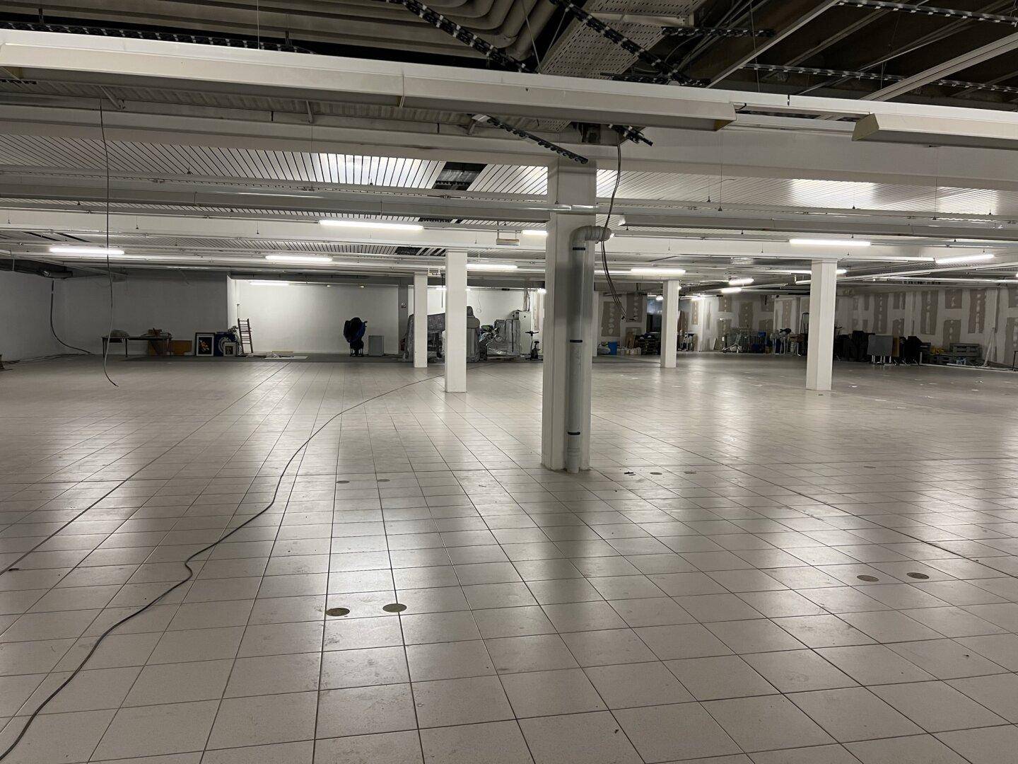 Großer, leerer Gewerberaum mit Fliesenboden, vielen Stützpfeilern und sichtbaren Deckeninstallationen.