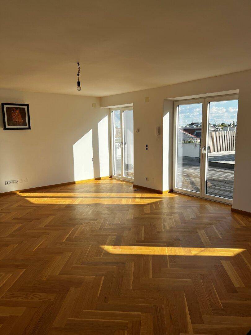 Heller Wohnraum mit Fischgrätparkett und Zugang zu einer großen Dachterrasse.