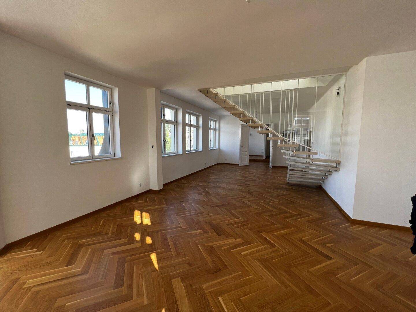 Helles Wohnzimmer mit elegantem Fischgrätparkett und einer modernen Treppe zum Obergeschoss.
