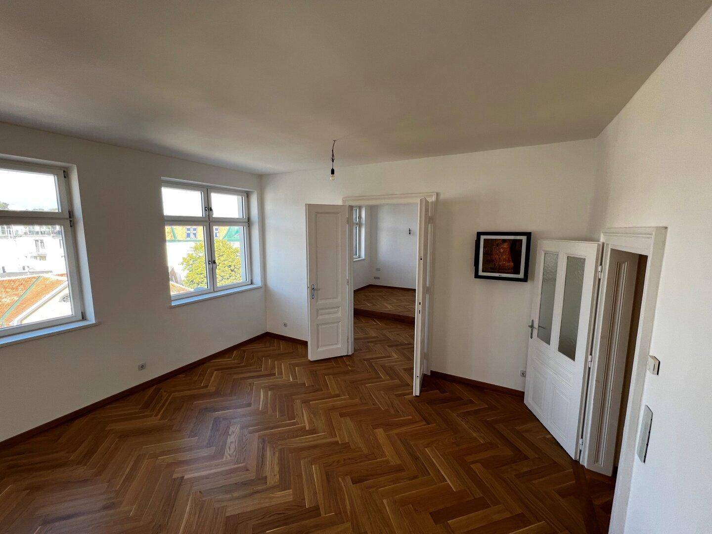 Geräumiger Wohnraum mit klassischem Fischgrätparkett und hohen Fenstern.