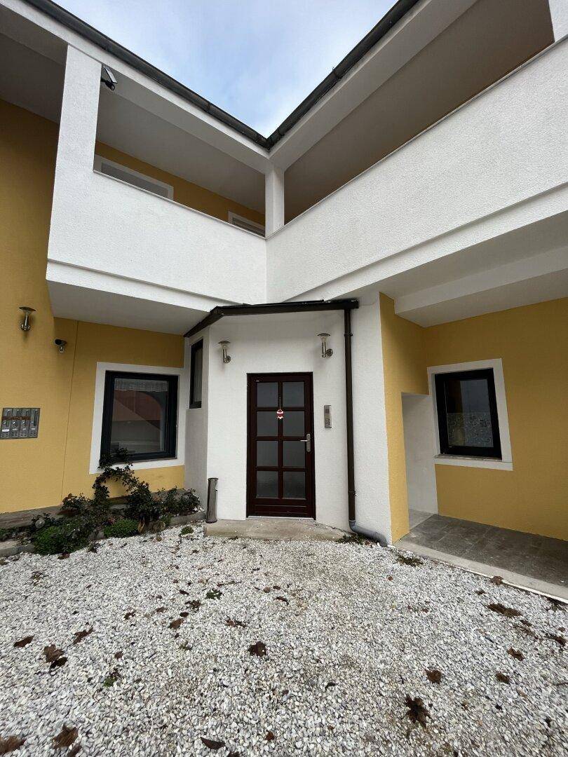 Haupteingang des Gebäudes mit gelber Fassade, dunkler Tür und Kiesfläche im Vordergrund.
