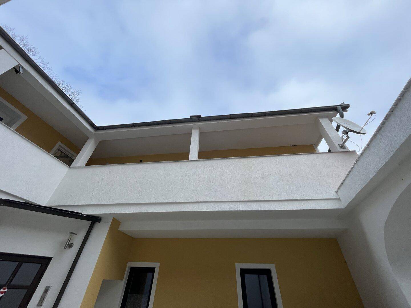 Außenansicht des Gebäudes mit gelber Fassade und weißem, überdachtem Balkonbereich.