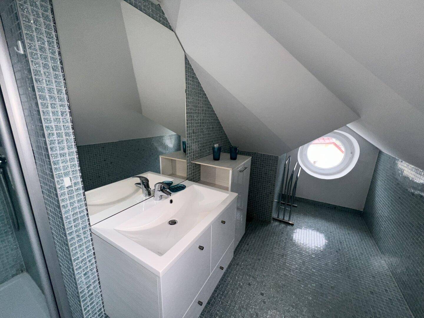 Helles Badezimmer im Dachgeschoss mit Waschtisch, großem Spiegel und blauen Mosaikfliesen.
