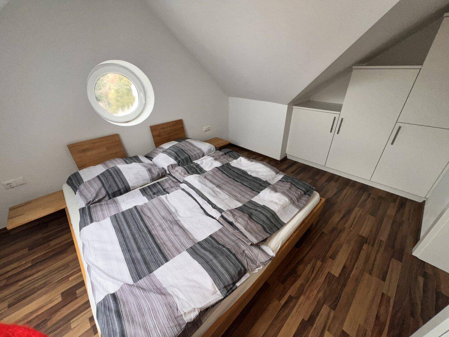 Schlafzimmer im Dachgeschoss mit Doppelbett, Einbauschränken und einem runden Fenster.