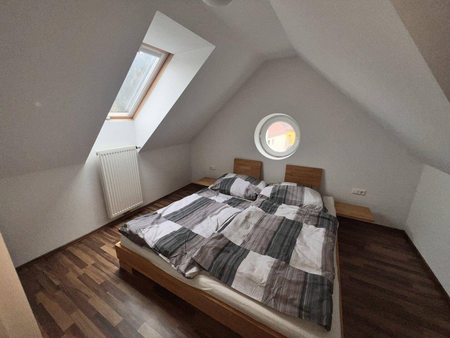 Geräumiges Schlafzimmer im Dachgeschoss mit Doppelbett, Dachfenster und dunklem Laminatboden.