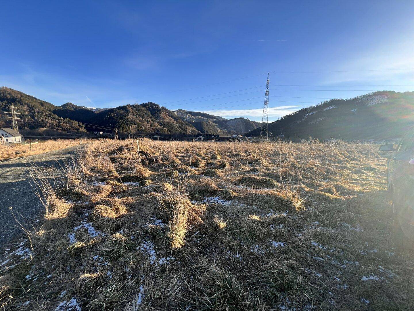 Weites offenes Feld mit trockenem Gras und Bergen im Hintergrund unter strahlend blauem Himmel.