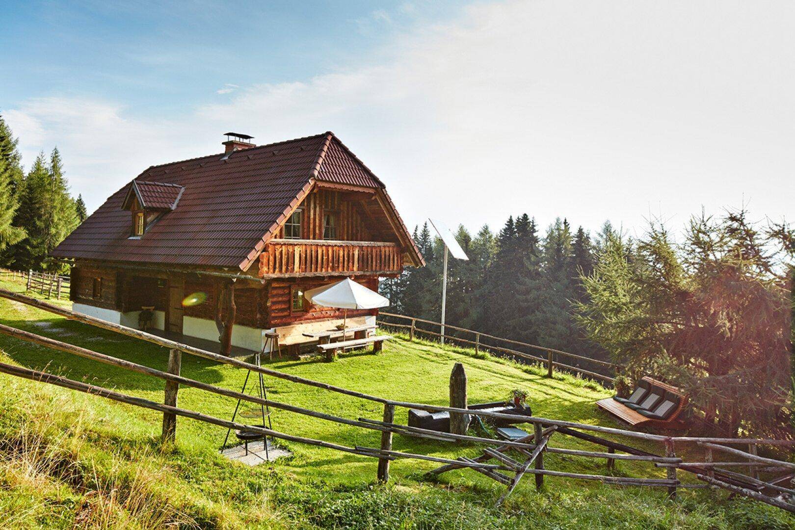 Rustikales Holzchalet mit Holzzaun und weitem Blick über die bewaldete Landschaft.