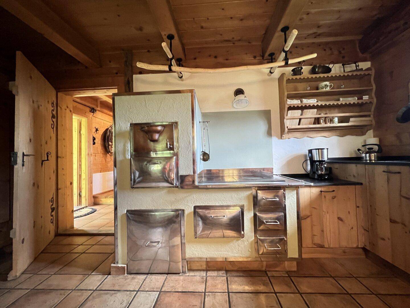 Rustikale Küche mit Holzbalken, gefliestem Boden und einem traditionellen Ofen mit Kupferdetails.
