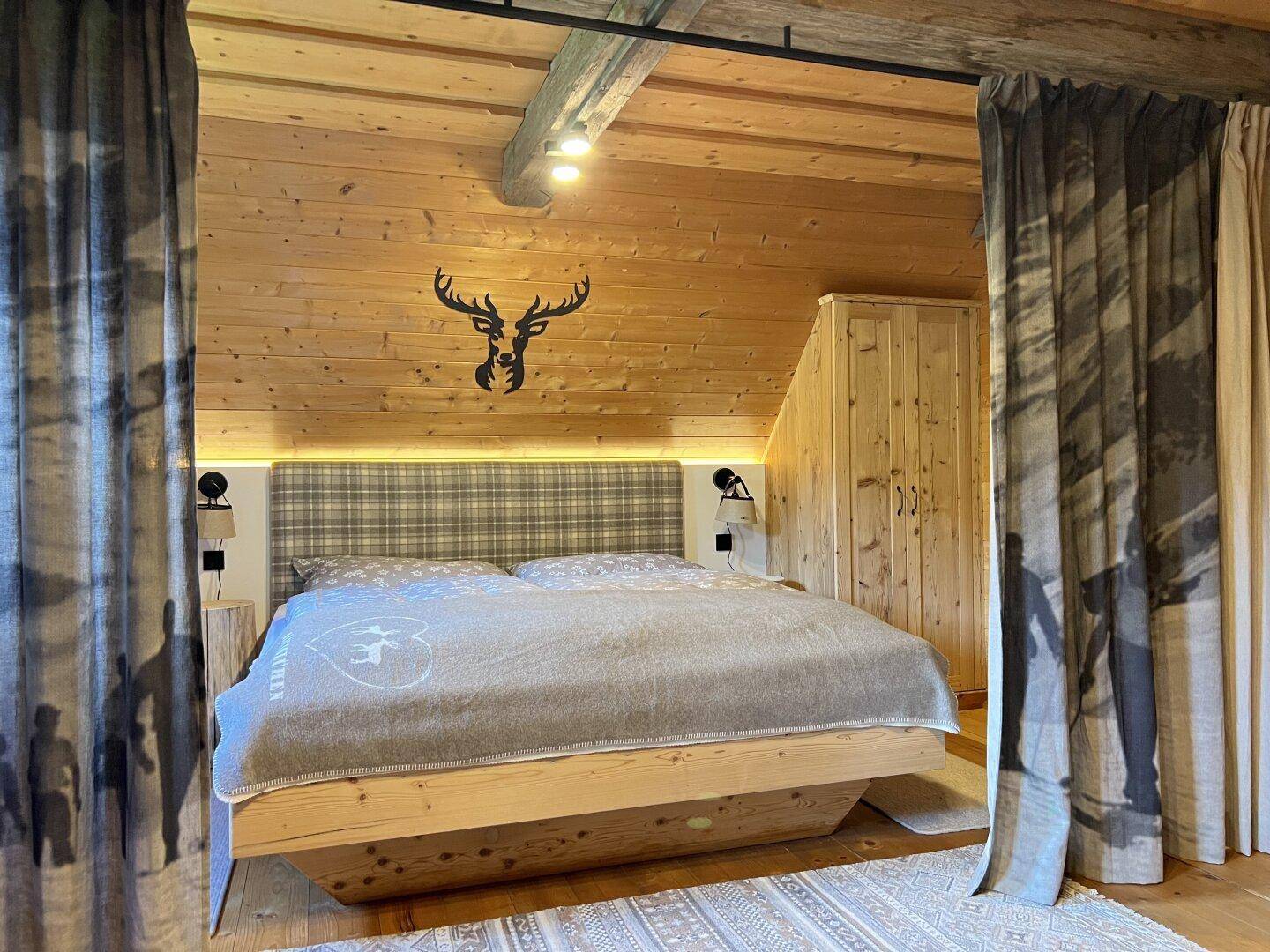 Schlafzimmer im alpinen Stil mit Holzwänden, schwebendem Bett und Hirschgeweih-Dekoration.