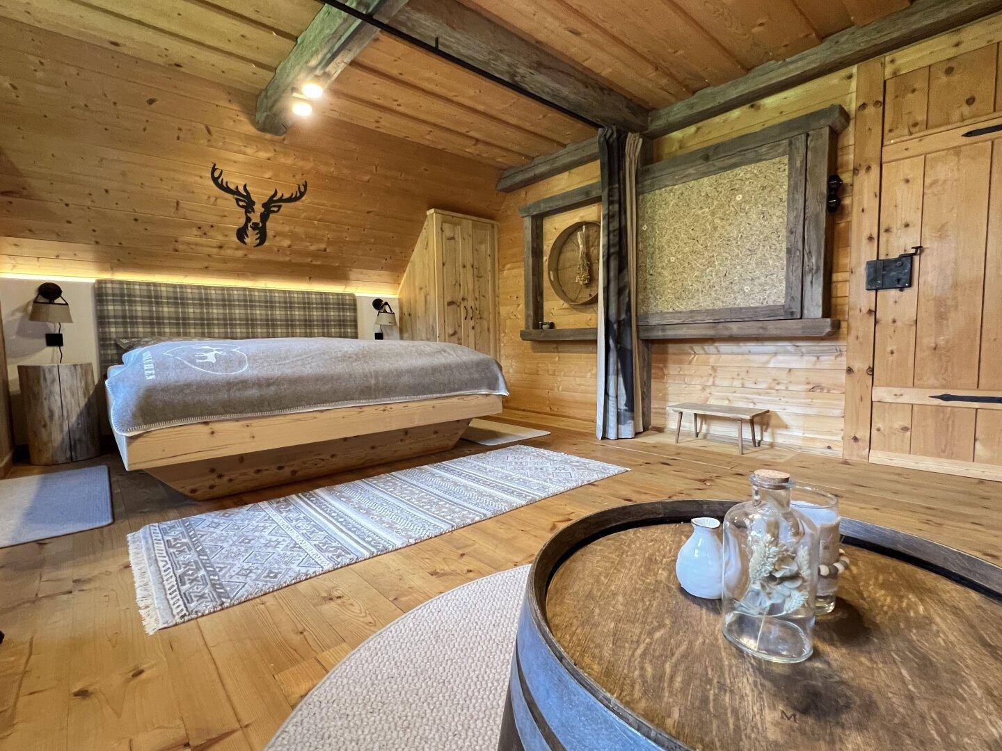Geräumiges Schlafzimmer mit Holzboden, Holzwänden und einem runden Couchtisch aus einem Weinfass.