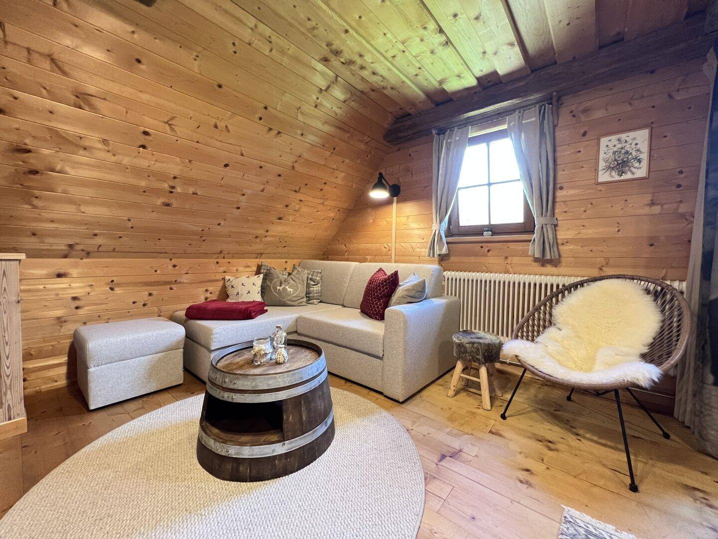 Gemütliches Wohnzimmer mit Holzwänden, bequemer Couch und einem Couchtisch aus einem Weinfass.