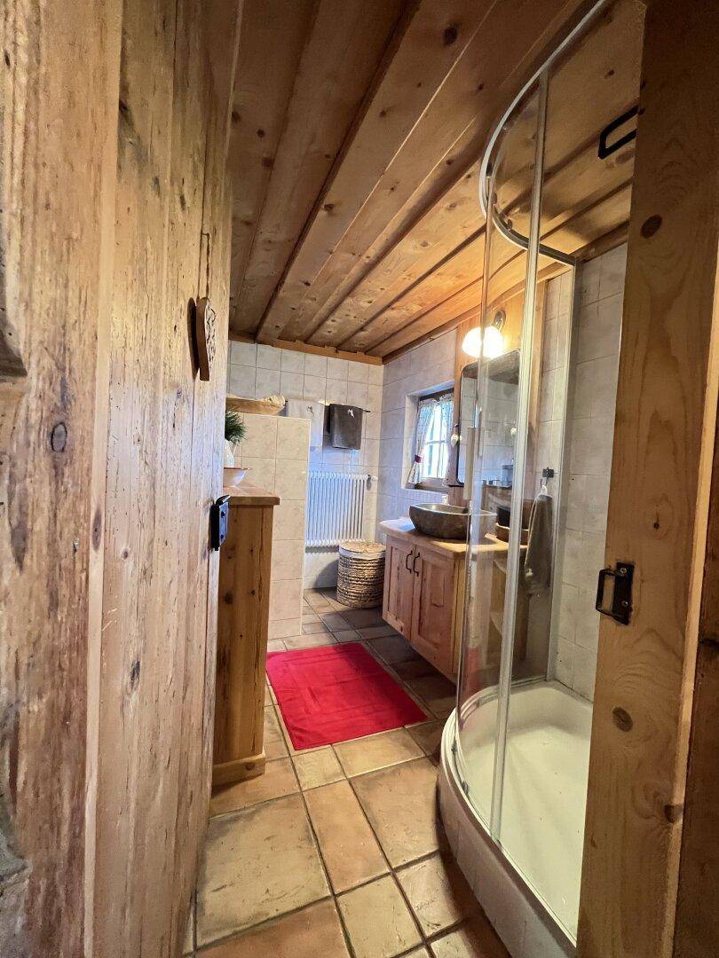 Schmaler Badezimmerbereich mit Holzwänden, Duschkabine und gefliestem Boden.