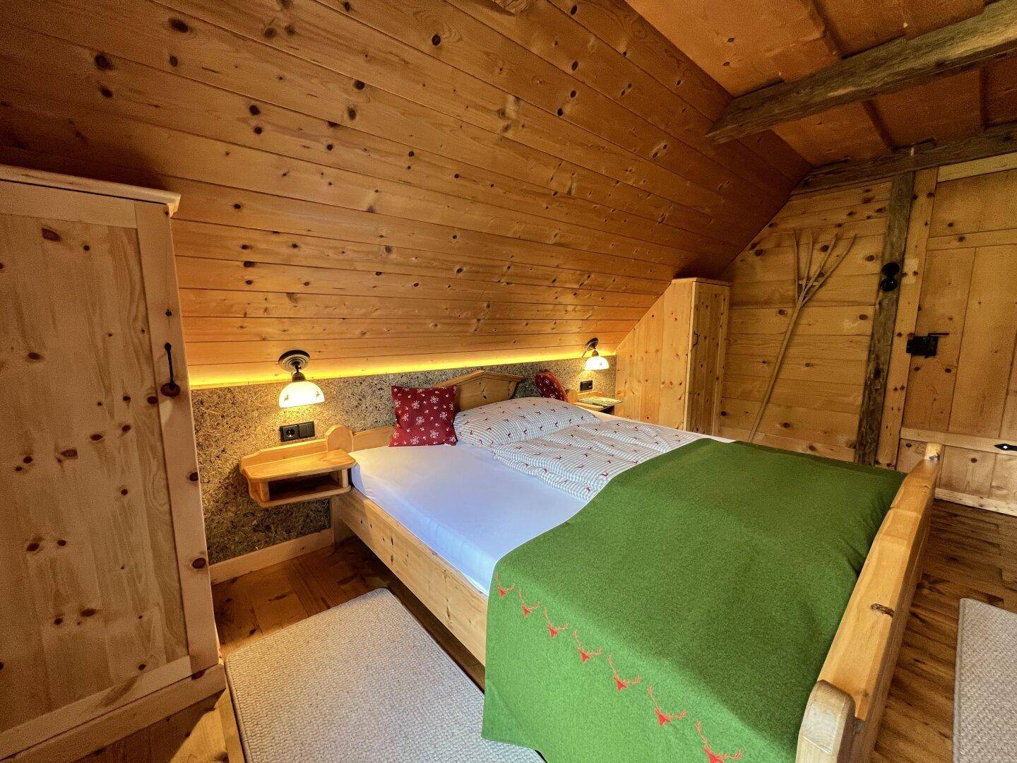 Gemütliches Schlafzimmer mit Holzwänden, Doppelbett und indirekter Beleuchtung unter der Dachschräge.
