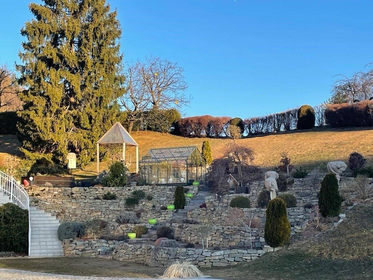 Weitläufiger Terrassengarten mit Steinmauern, Treppen, einem Gewächshaus und einem Pavillon.