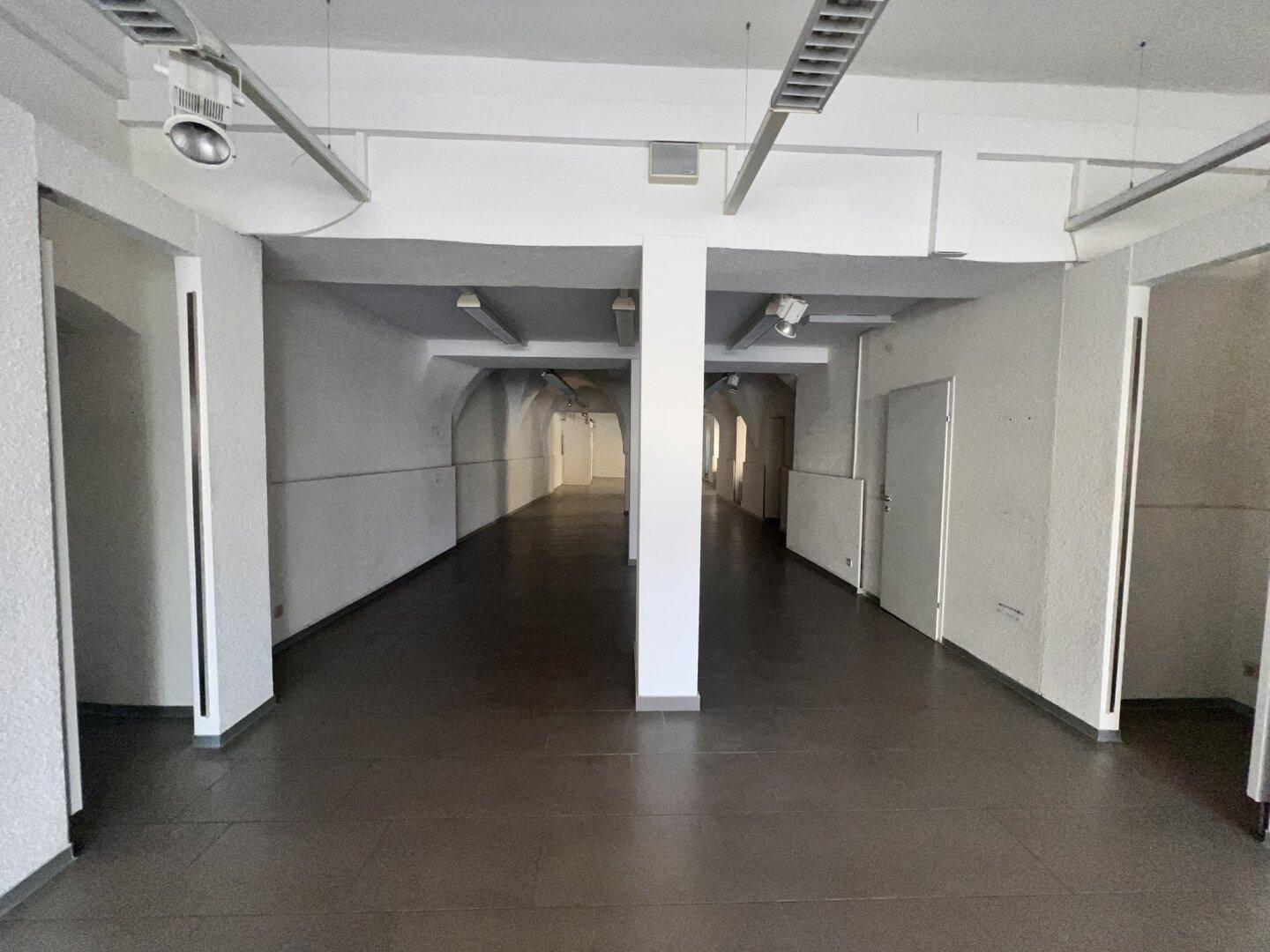 Geräumiger Gewerberaum mit Säulen und dunklem Fliesenboden, der sich für verschiedene Geschäftskonzepte eignet.