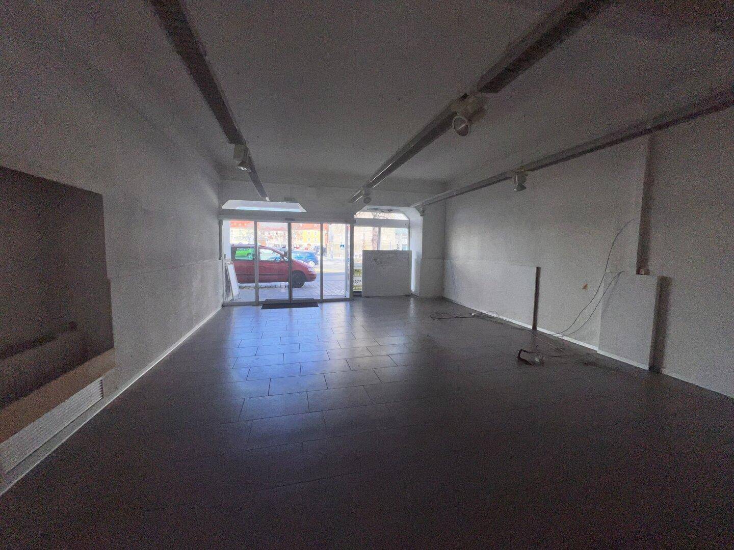 Leerer Gewerberaum mit dunklen Fliesen und großen Schaufenstern zur Straße hin, bereit für neue Gestaltung.