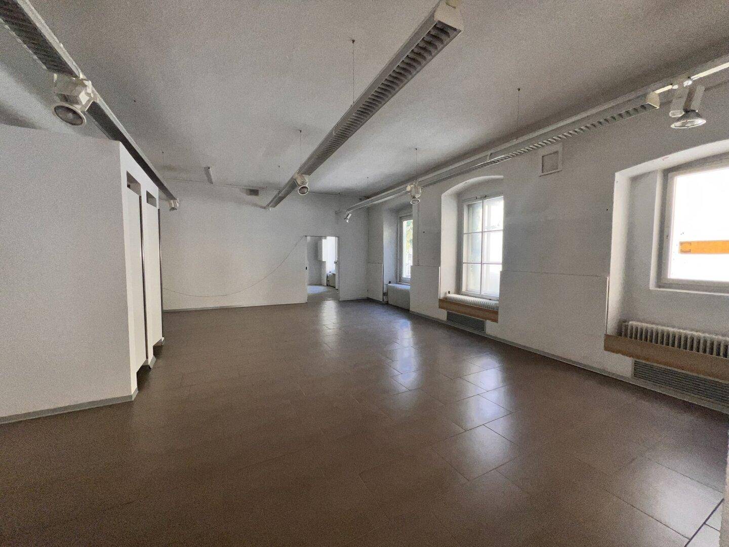 Heller, leerer Gewerberaum mit dunklem Fliesenboden, weißen Wänden und traditionellen Fenstern.
