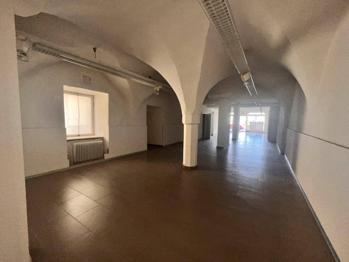 Historischer Gewerberaum mit eleganten Gewölbedecken, Säulen und einem Fenster, das Tageslicht hereinlässt.
