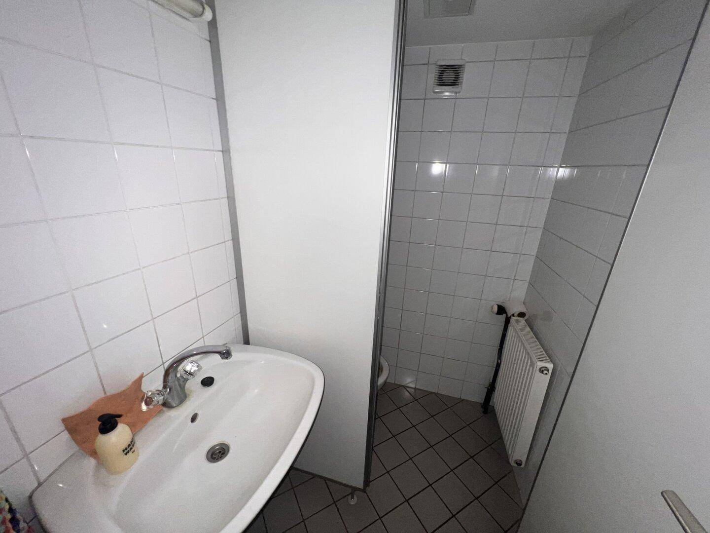 Kleines Badezimmer mit weißen Fliesen, einem Waschbecken und einer Duschkabine, funktional und sauber.