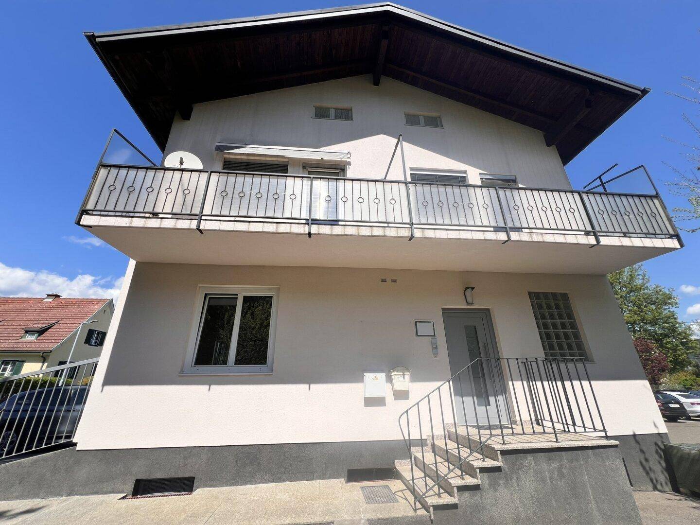Vorderansicht eines Mehrfamilienhauses mit einem großen Balkon und einer Außentreppe zum Eingang.