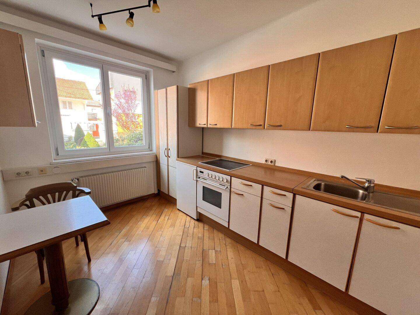 Helle Küche mit Fenster, Holzboden und einem kleinen Essbereich, ideal für schnelle Mahlzeiten.