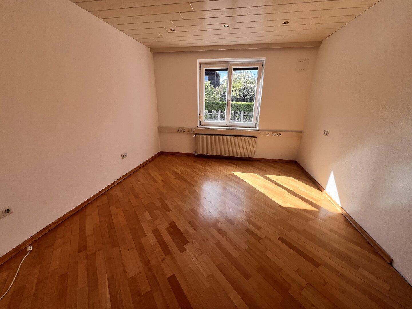 Ein weiterer heller Büroraum mit Holzboden und einem Fenster, das den Blick ins Grüne freigibt.