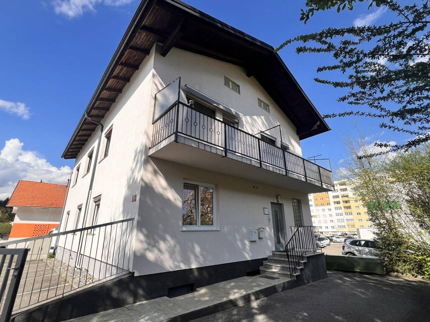 Seitenansicht des Gebäudes mit Balkon und Blick auf den Parkplatz und die Umgebung.
