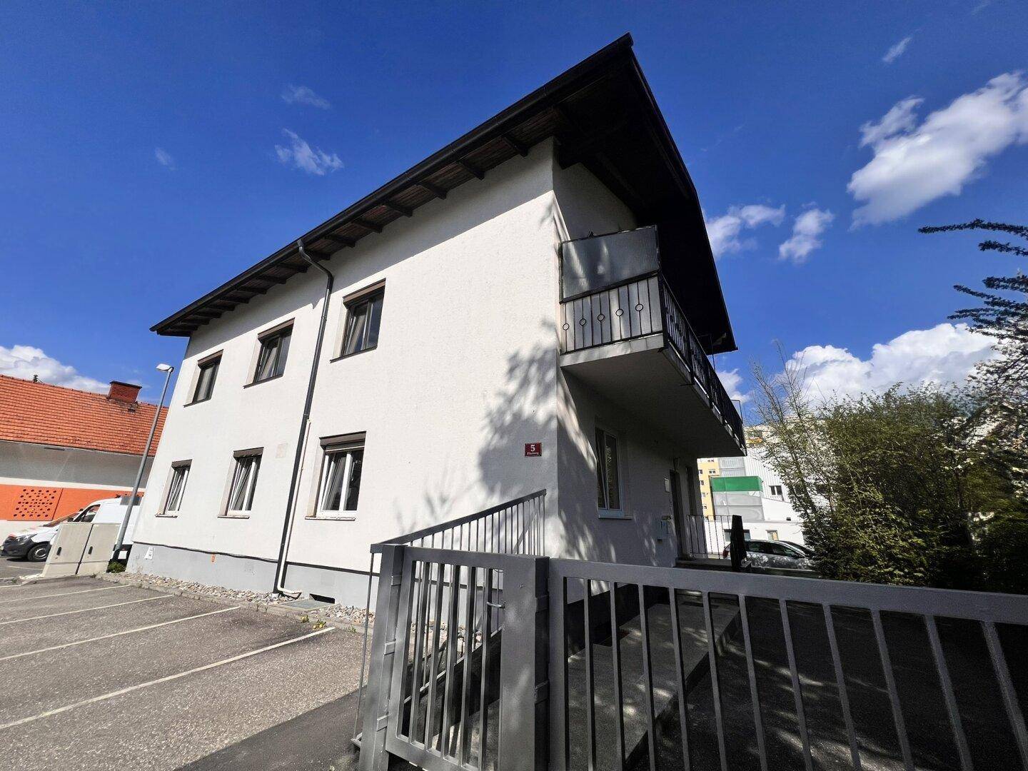 Seitenansicht des Gebäudes mit mehreren Fenstern und einem Balkon, umgeben von einem Zaun.