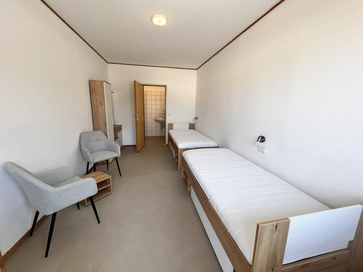 Geräumiges Schlafzimmer mit zwei Einzelbetten, Sitzgelegenheiten und Zugang zu einem gefliesten Bad.