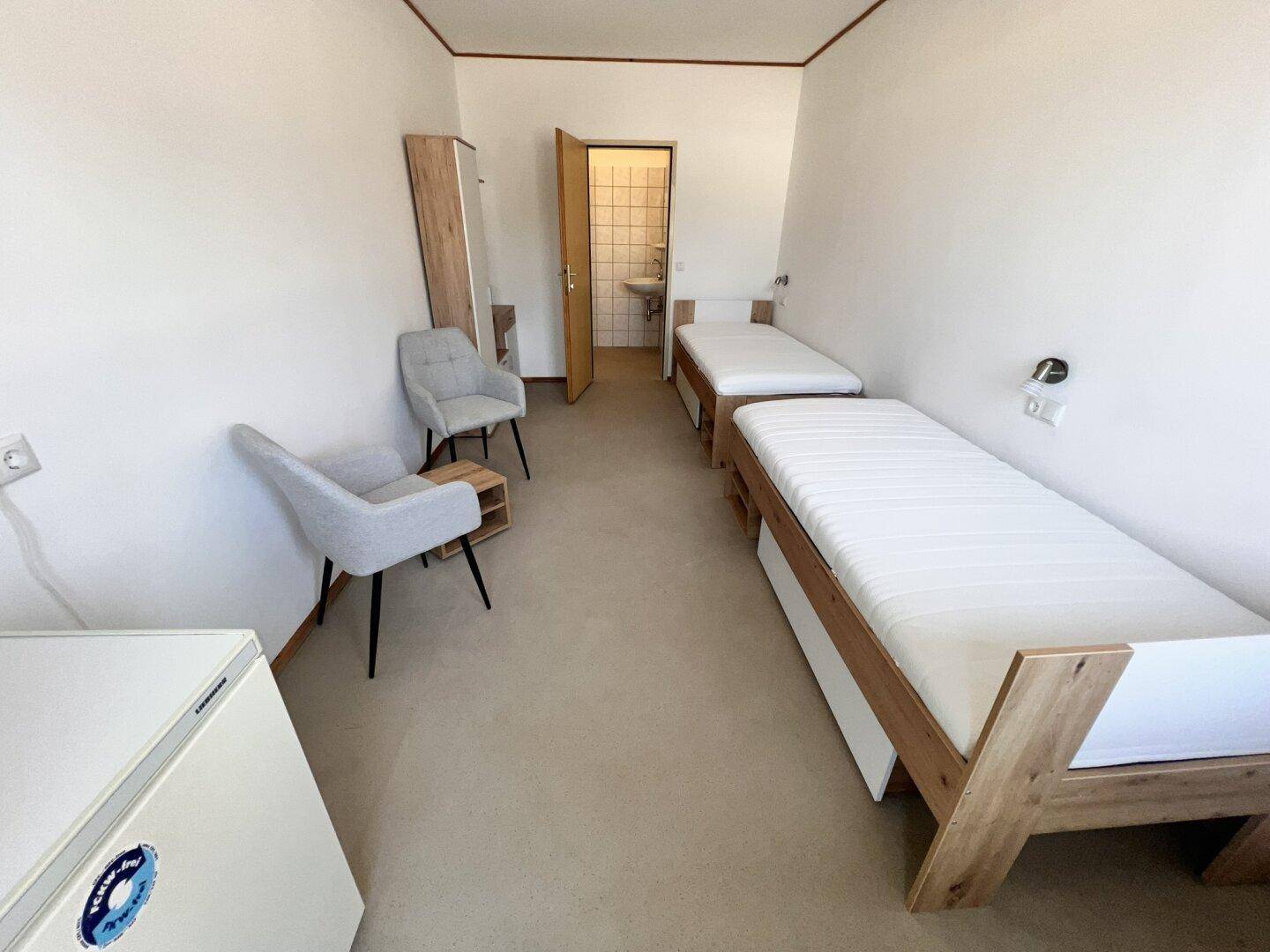 Schlafzimmer mit zwei Einzelbetten, einem Kleiderschrank und Zugang zu einem gefliesten Badezimmer.