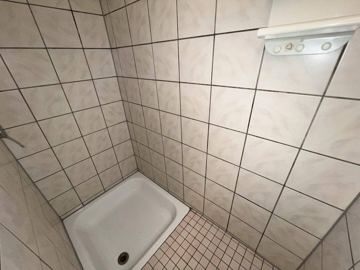 Duschbereich mit weißen Fliesen und einer Duschwanne, Teil eines funktionalen Badezimmers.