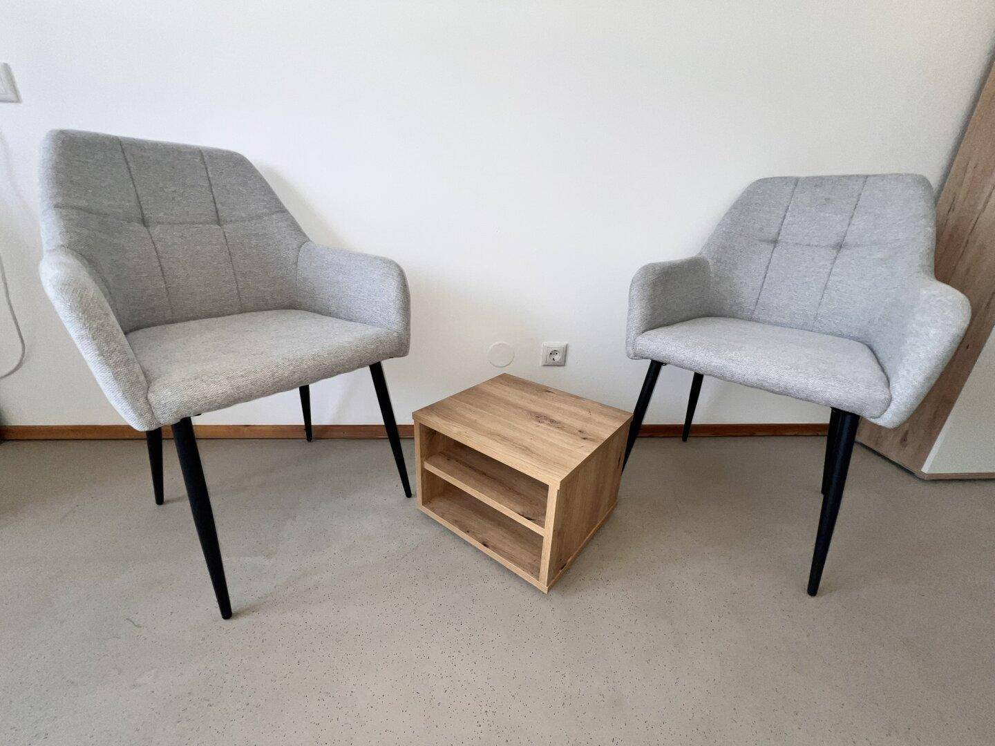 Zwei moderne, gepolsterte Sessel mit einem kleinen Holztisch als Ablagefläche.