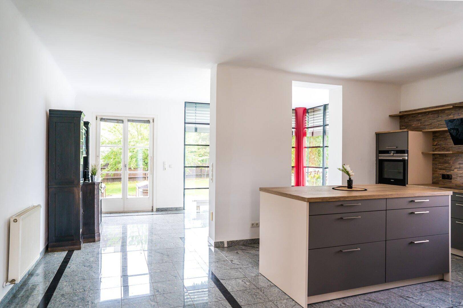 Moderne Küche mit Kücheninsel und Blick durch die Glasfront in den angrenzenden Raum.