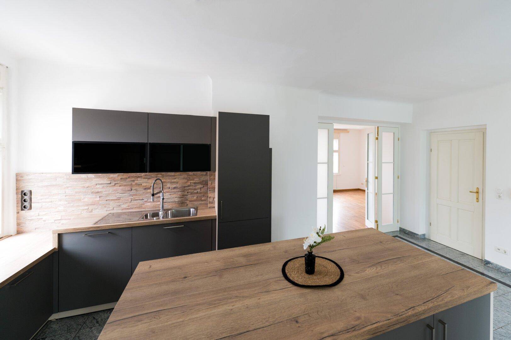 Stilvolle Küche mit dunklen Schränken, Holz-Arbeitsplatte und Steinwand-Rückwand.