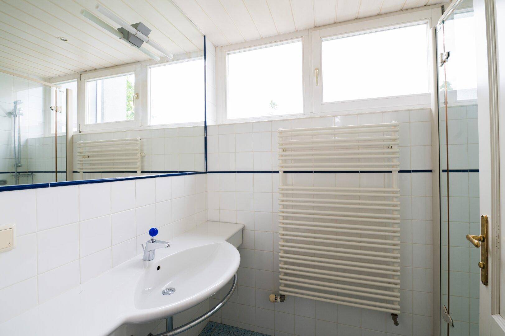 Helles Badezimmer mit weiß gefliesten Wänden, Waschbecken und beheiztem Handtuchhalter.