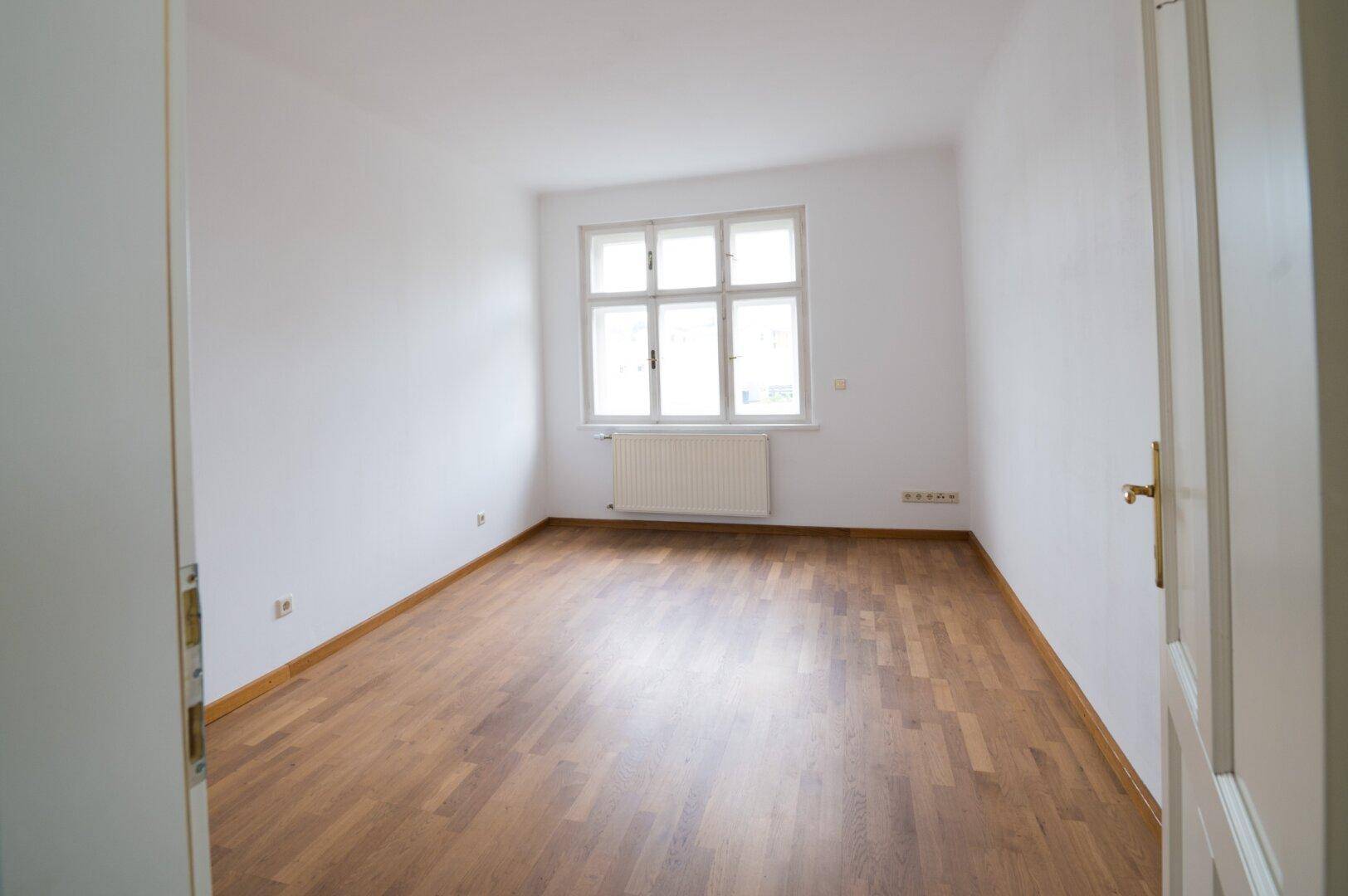 Geräumiges Schlafzimmer mit Holzboden und einem großen Fenster, das viel Licht spendet.