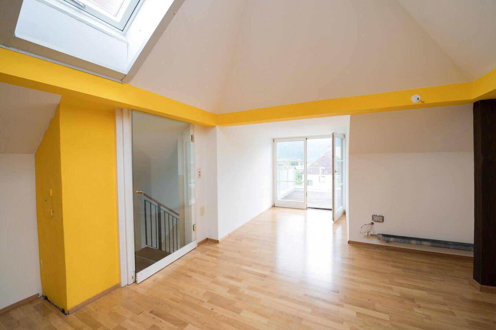 Helles Dachgeschosszimmer mit Holzboden, Dachfenster und Zugang zu einem Balkon.