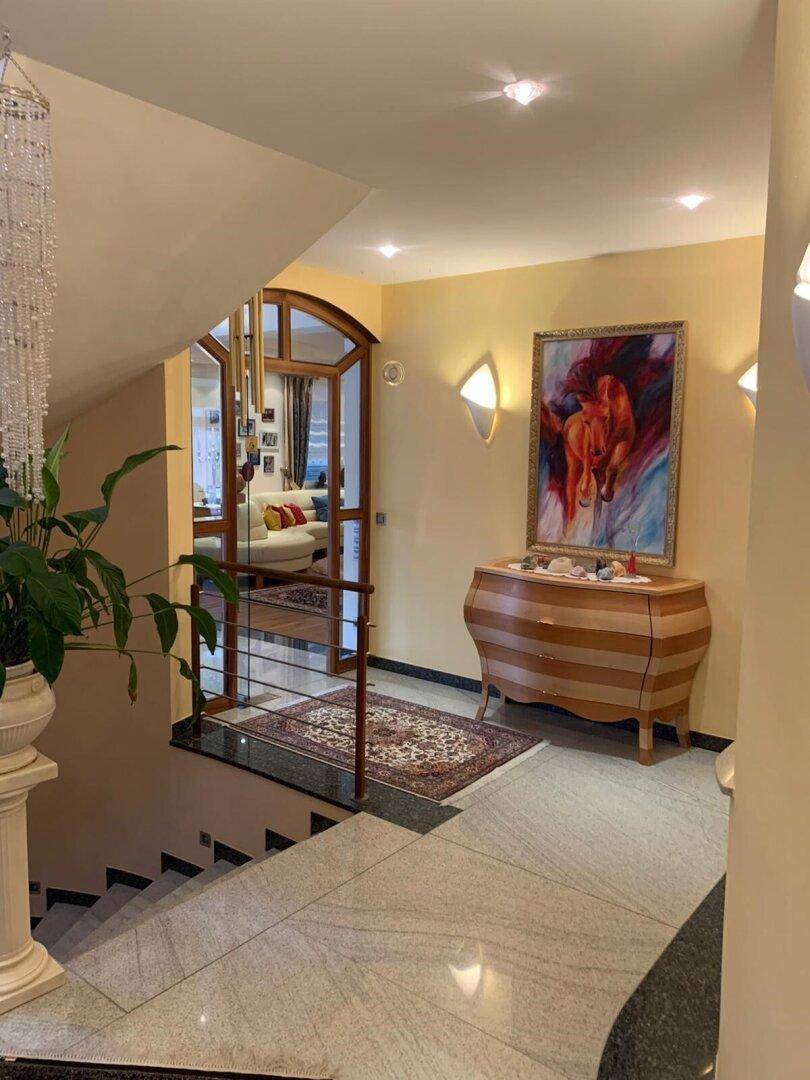 Geräumiger Treppenabsatz mit eleganter Kommode, Kunstwerk und Blick in den Wohnbereich.
