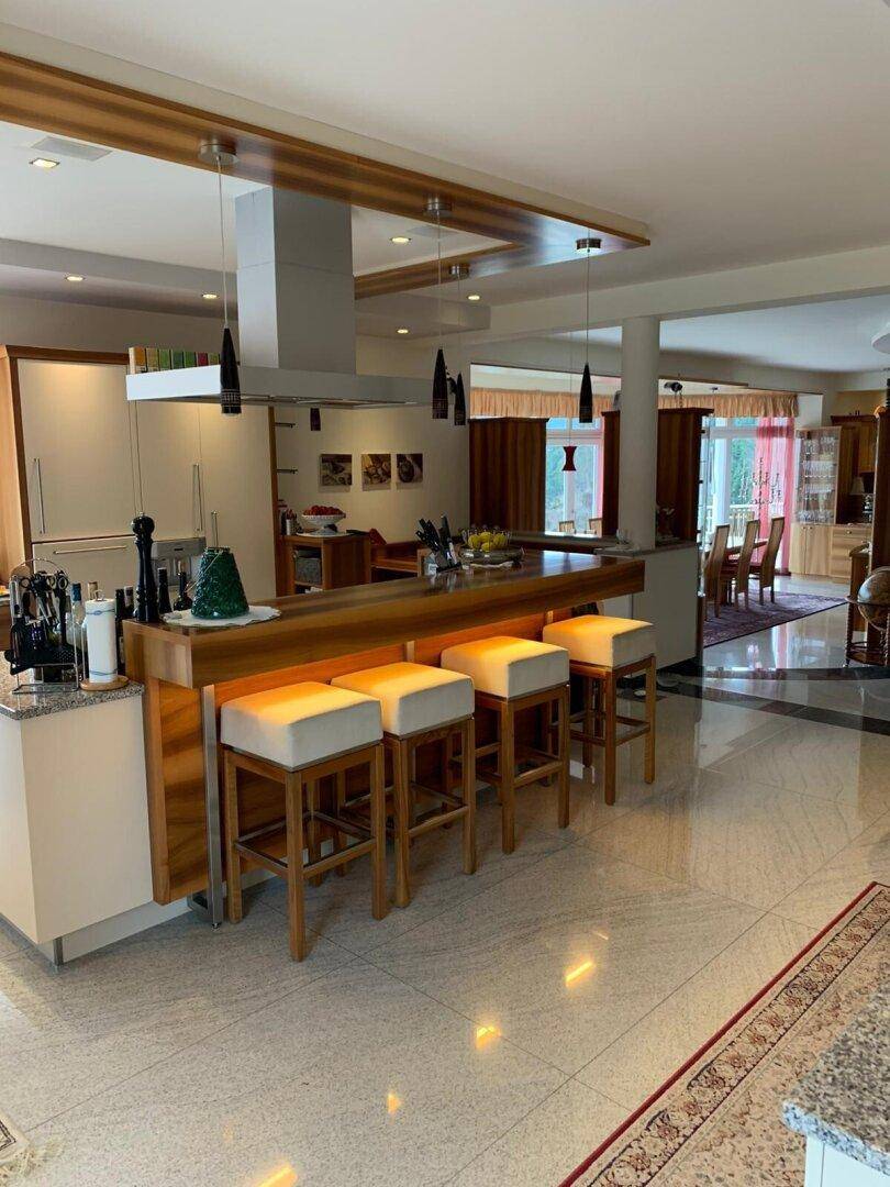 Moderne offene Küche mit großer Kücheninsel, Frühstücksbar und Essbereich im Hintergrund.