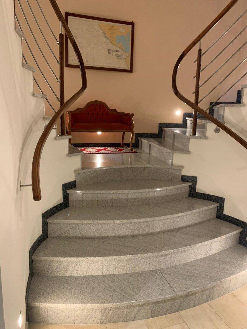 Elegante geschwungene Treppe mit Granitstufen und modernem Geländer in einem Flurbereich.