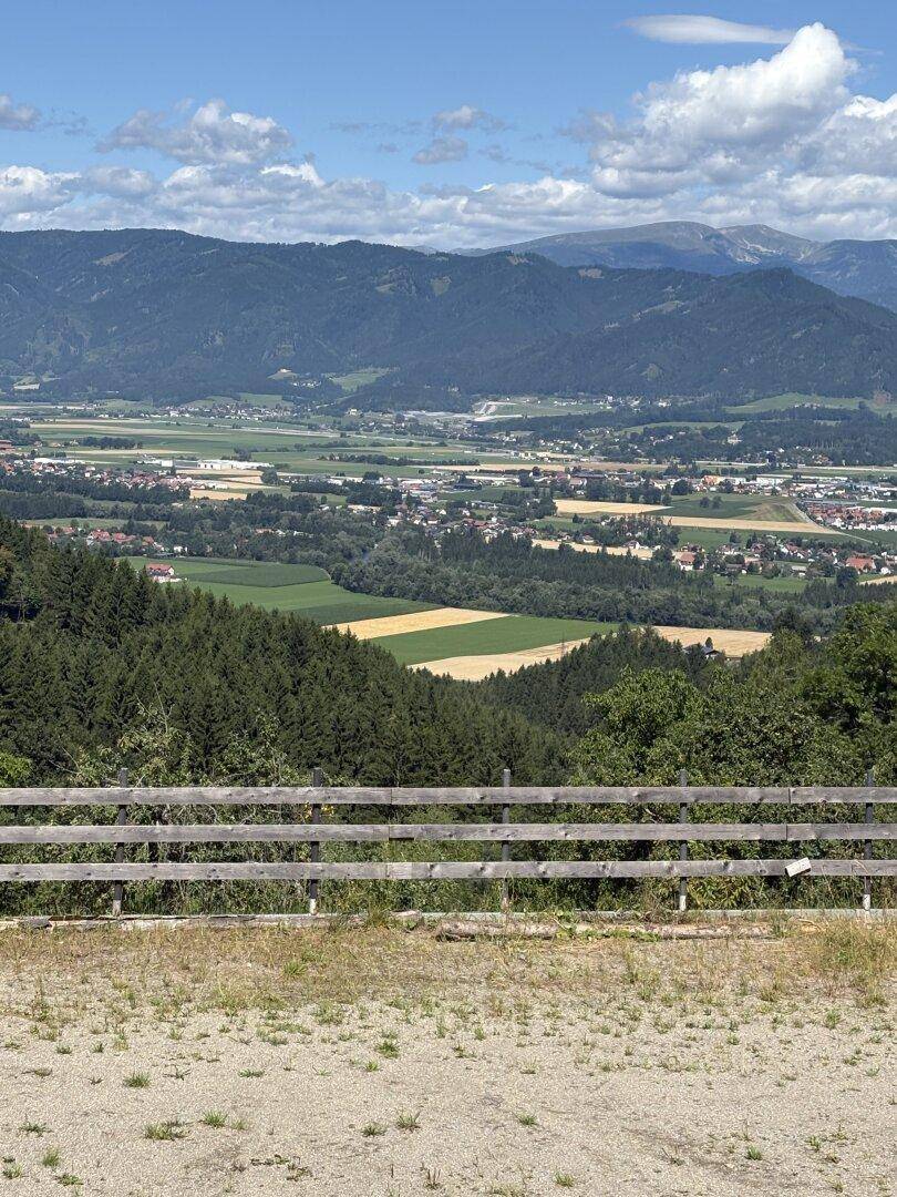 Weitläufiger Blick über ein Tal mit einer Stadt, Feldern und Bergen am Horizont.