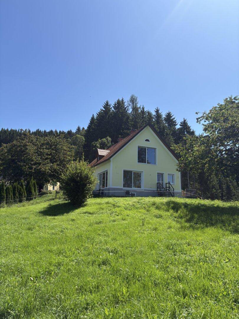 Freistehendes Haus mit hellgelber Fassade und rotem Satteldach, umgeben von grüner Natur.