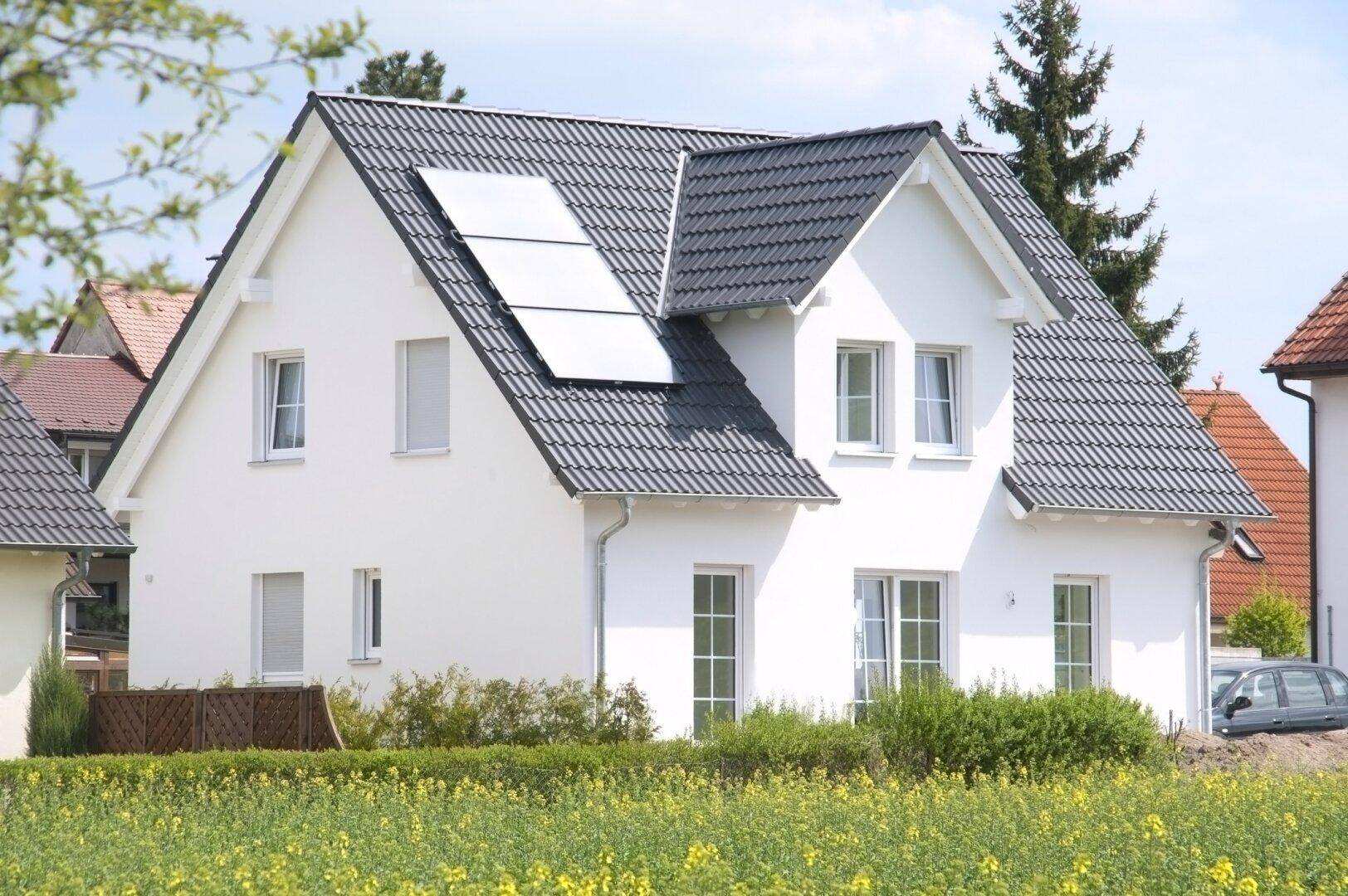 Weißes Einfamilienhaus mit Satteldach und Photovoltaikanlage, umgeben von grünen Feldern.