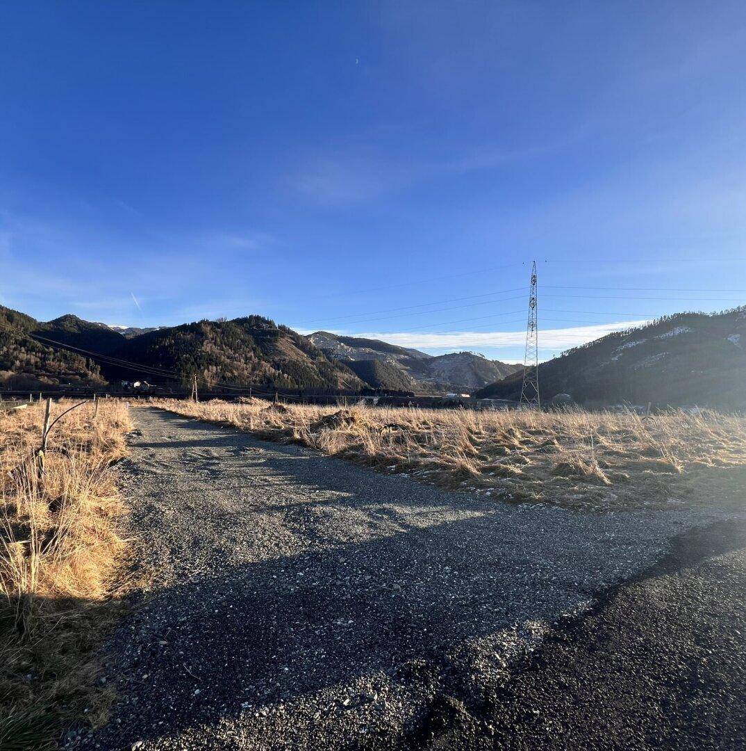 Weitläufige Landschaft mit Bergen und einem Feldweg unter einem klaren blauen Himmel.