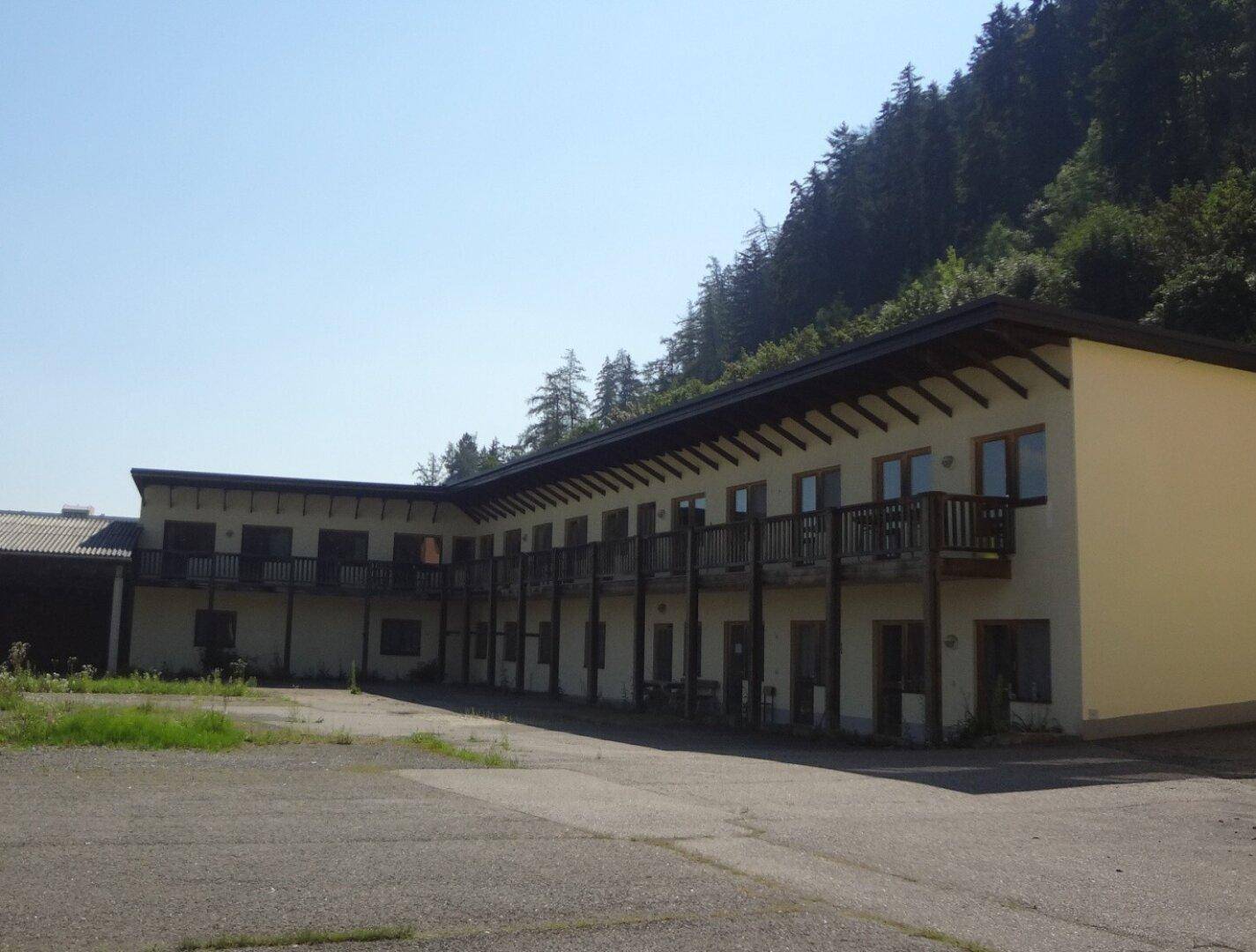 Gebäude mit mehreren Balkonen und Blick auf bewaldete Hügel in alpiner Umgebung.