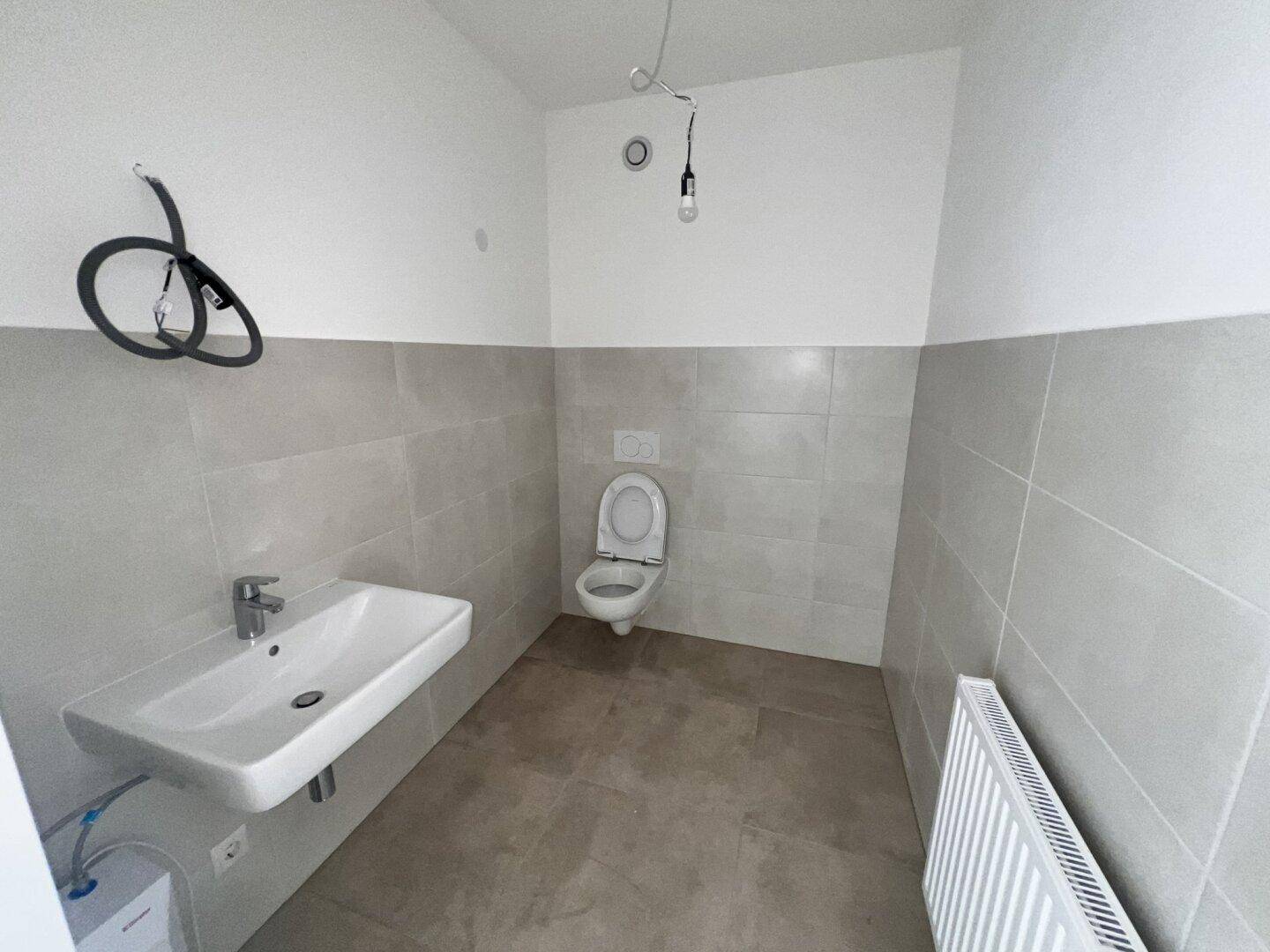Modernes WC mit wandhängender Toilette, Waschbecken und grauen Fliesen, noch im Ausbau.