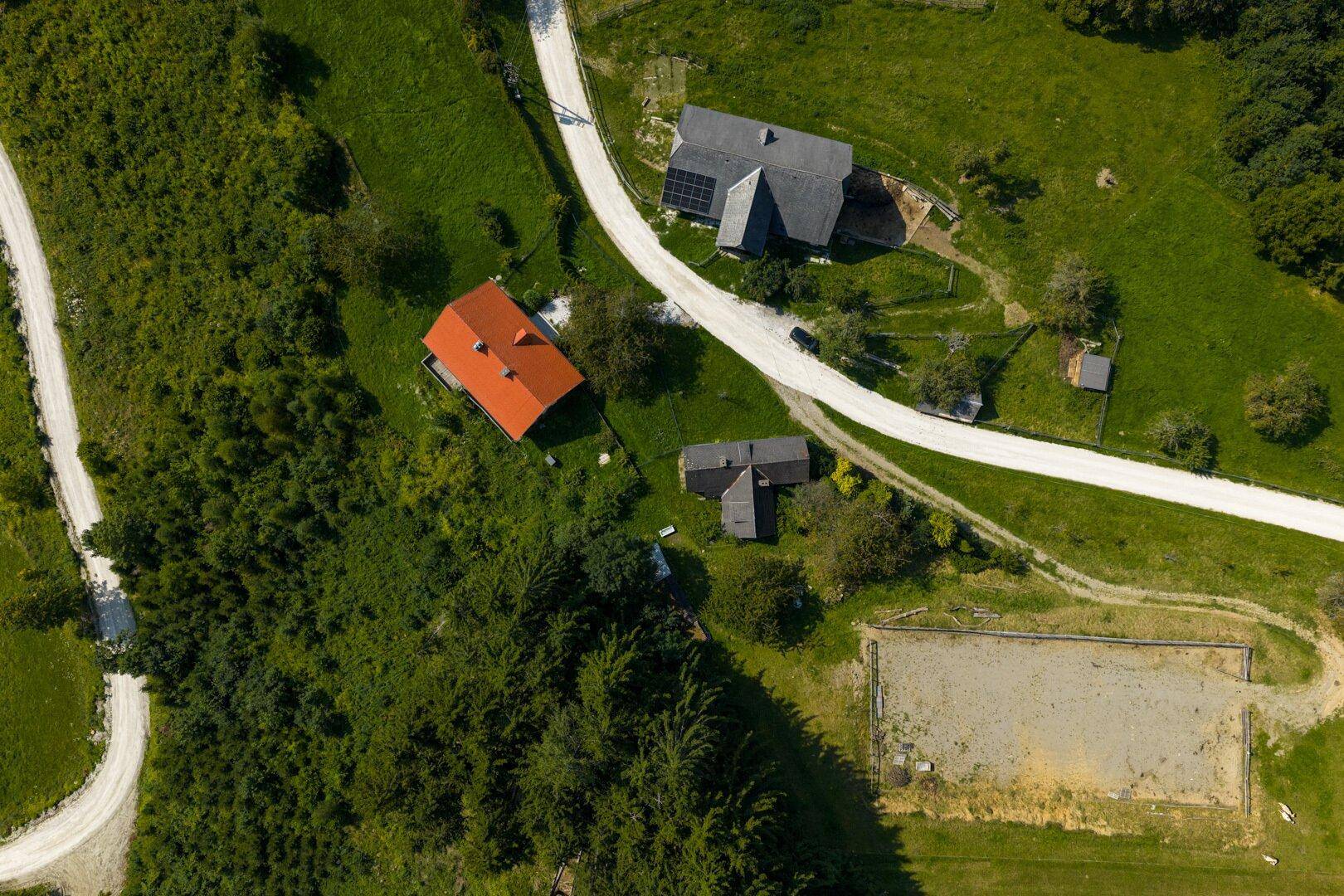 Detaillierte Luftaufnahme eines ländlichen Anwesens mit Gebäuden, Zufahrt und einem Reitplatz.
