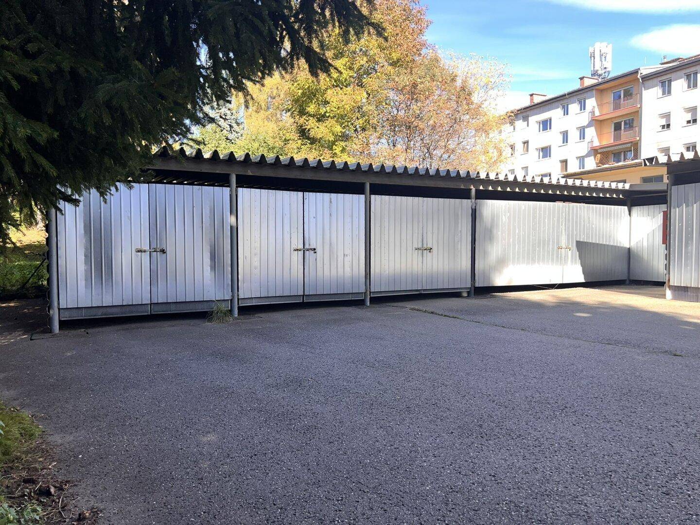 Mehrere Garagenboxen aus Metall mit Schwingtoren und einem asphaltierten Vorplatz.