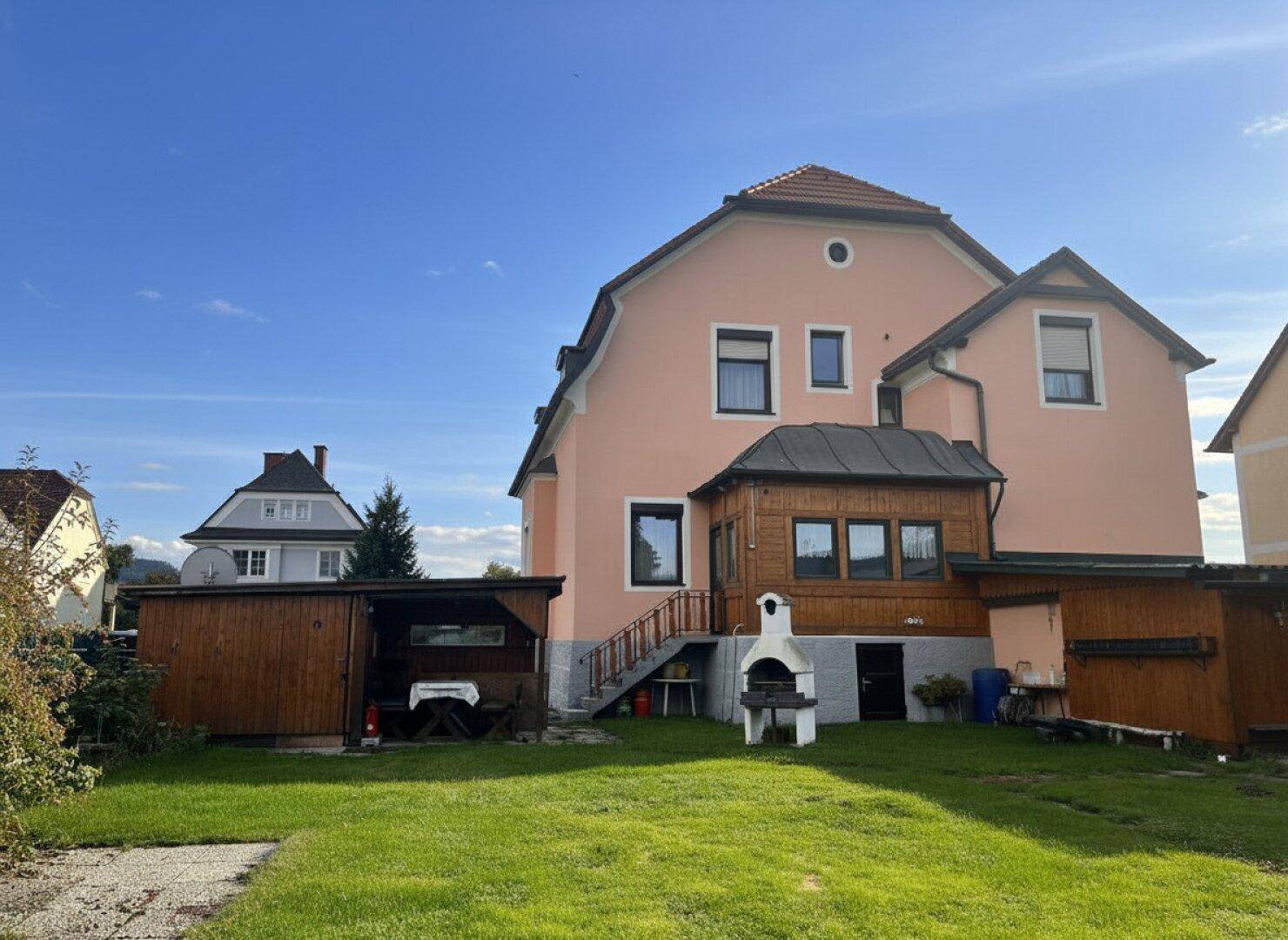 Geräumiger Gartenbereich hinter dem Haus mit Rasenfläche, Grillplatz und Zugang zu einer überdachten Terrasse.
